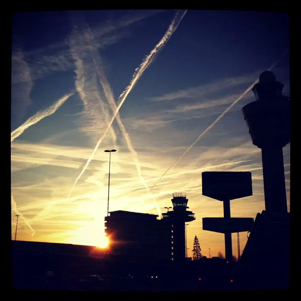 Airport control tower in silhouette at sunrise, with crossing contrails in the sky