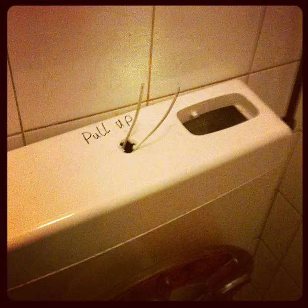 A toilet cistern with a handwritten 'Pull up' and two loose wires where the flush handle should be