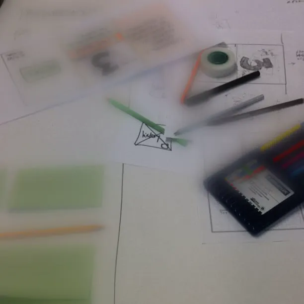 Paper sketches, coloured pencils and a phone on a desk