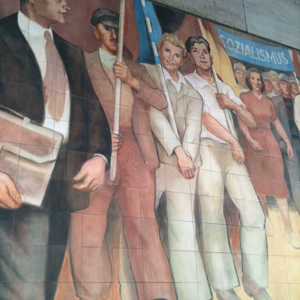 Mural de azulejos en Berlín con trabajadores marchando con banderas bajo la palabra Sozialismus