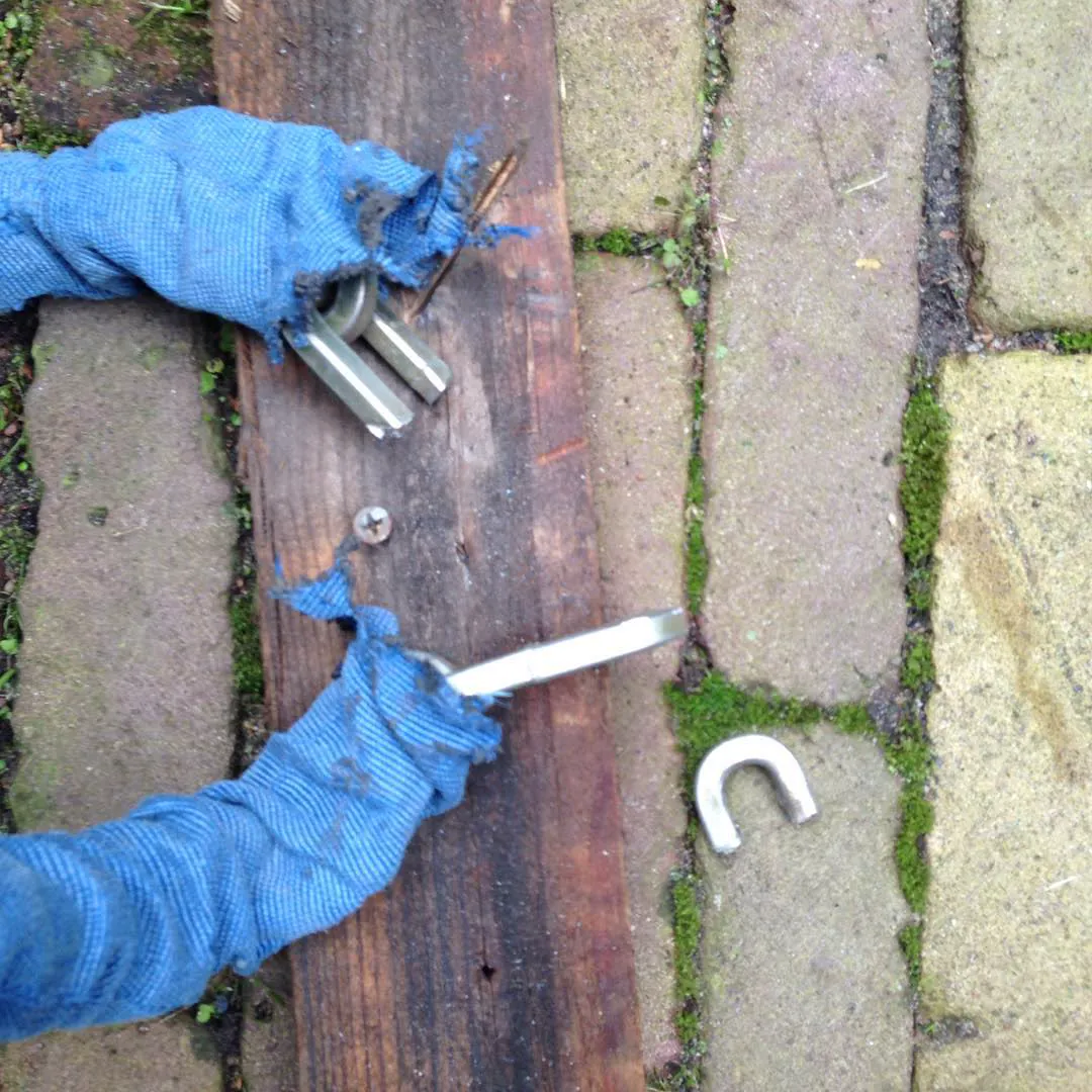 Pliers wrapped in blue cloth, a cut lock and screws on a wooden plank on the pavement