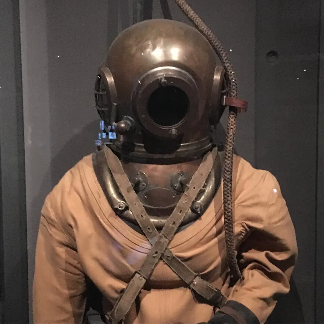 A vintage copper diving helmet and canvas suit on display