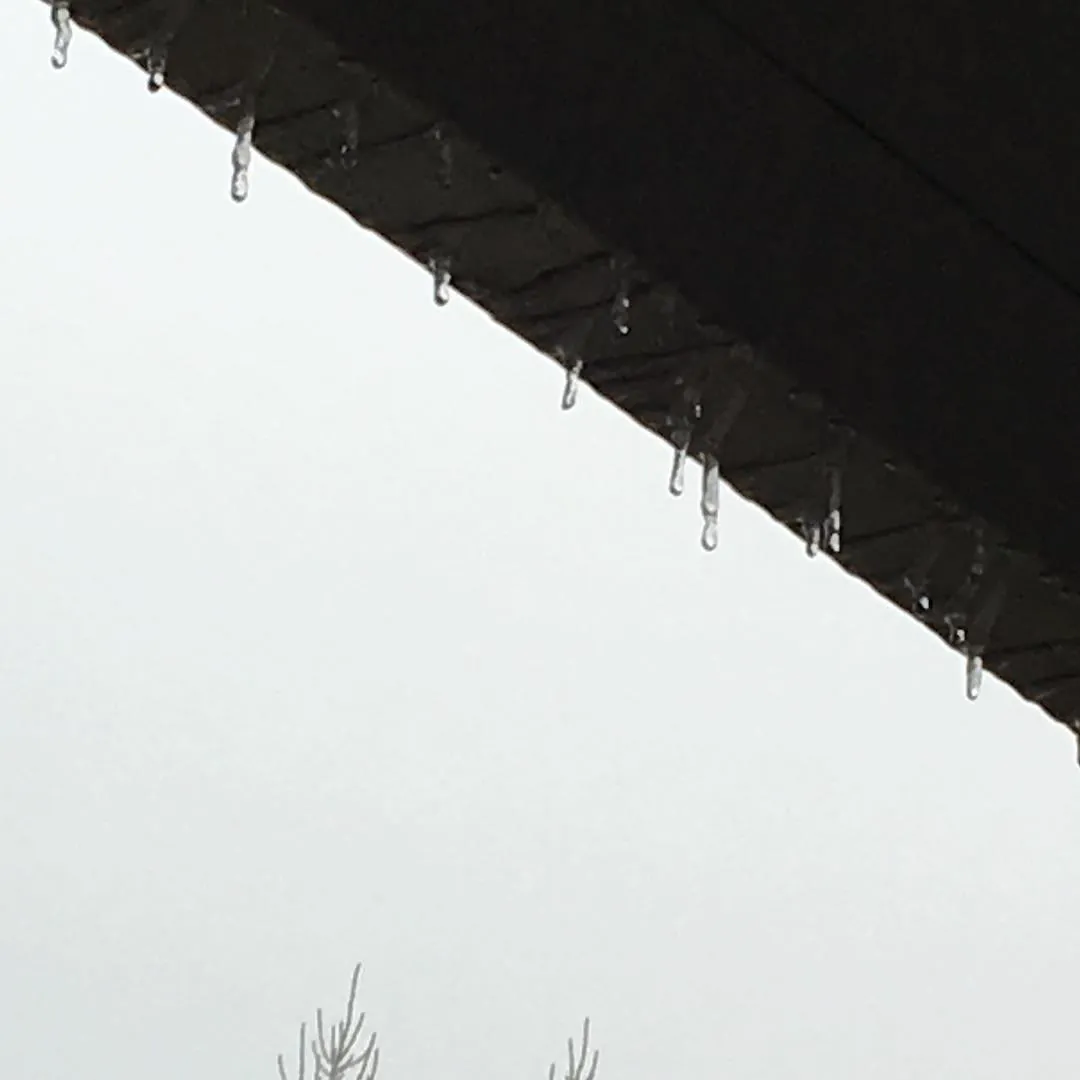 Icicles forming along a roof edge against a white sky