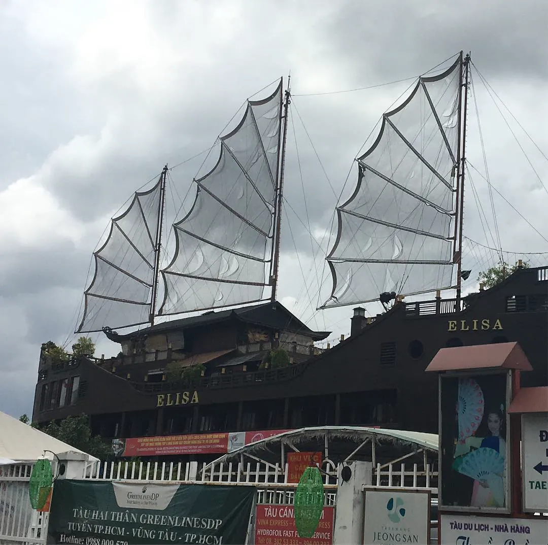 The Elisa, a restaurant ship with tall junk sails, on the Saigon river under grey clouds