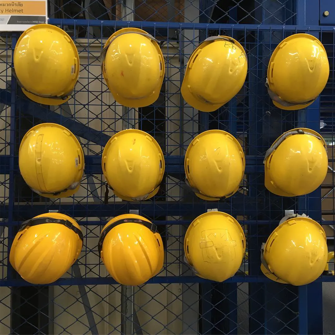 Yellow hard hats hanging in neat rows on a blue mesh rack