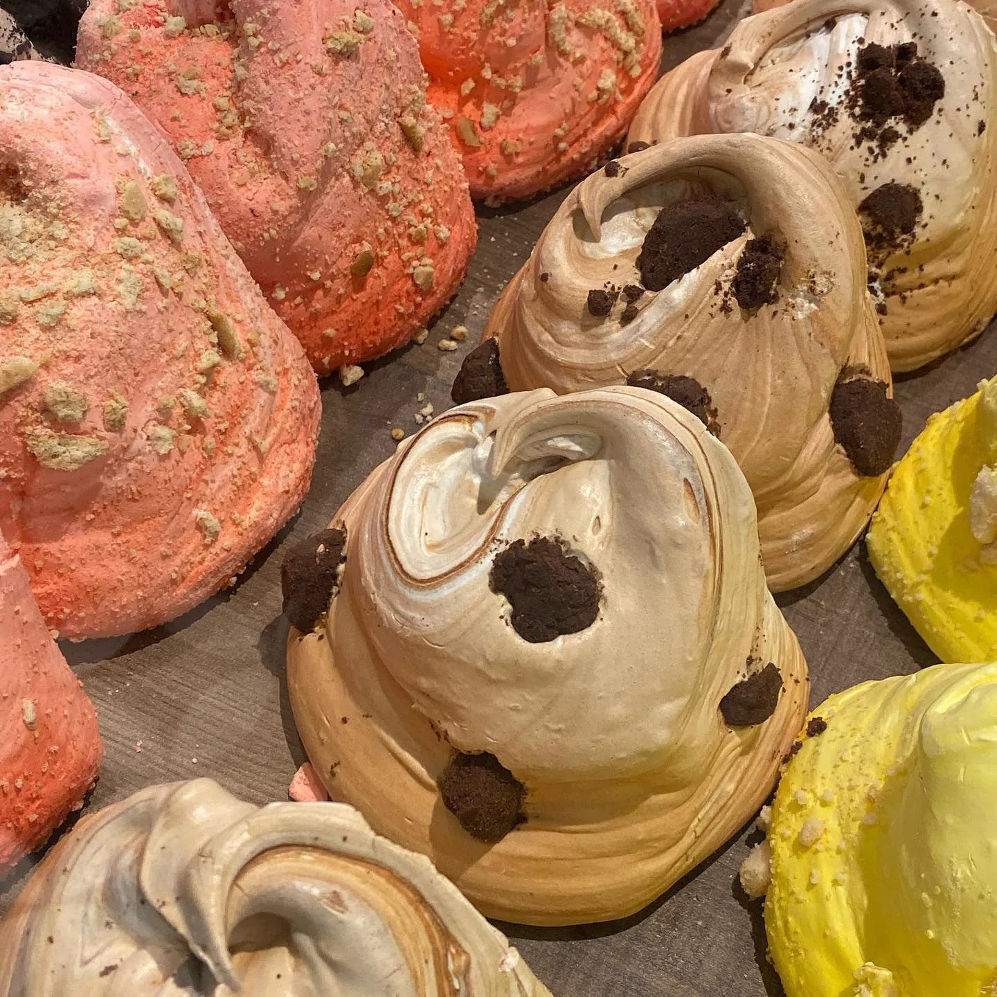Rows of large meringues in pastel colours, topped with crumbled biscuit
