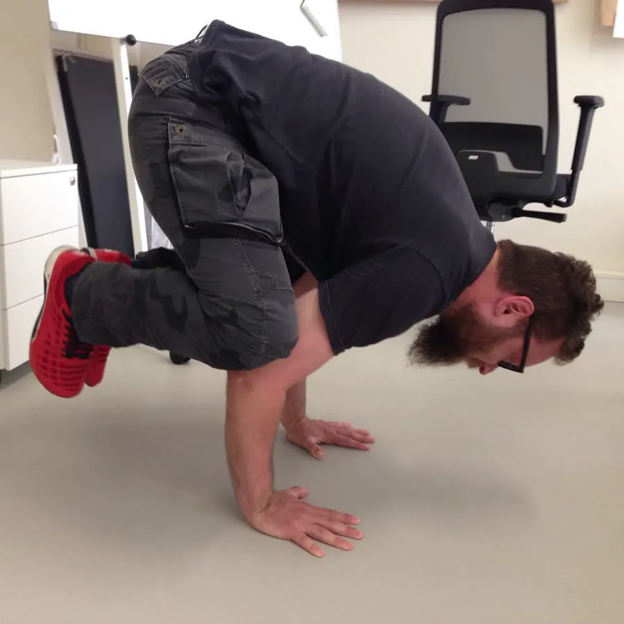 Natan in crow pose, balancing on his hands on an office floor